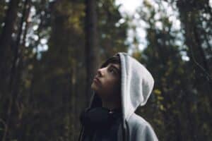 teen boy wearing bray hoodie looking up into trees contemplating self-harm